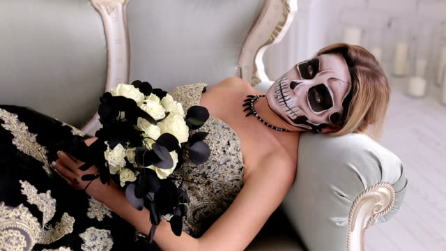 A-creepy-woman-with-makeup-in-the-form-of-a-skull-lies-on-a-retro-sofa.Halloween