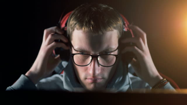 Ein-Mann-setzt-Kopfhörer-auf-und-beginnt-zu-sprechen,-während-er-den-Computer-spielt