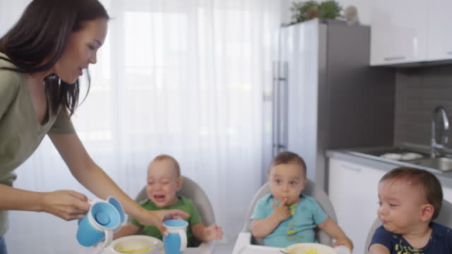 Junge-Mutter-gibt-Sippy-Tassen,-um-Messy-Baby-Triplets