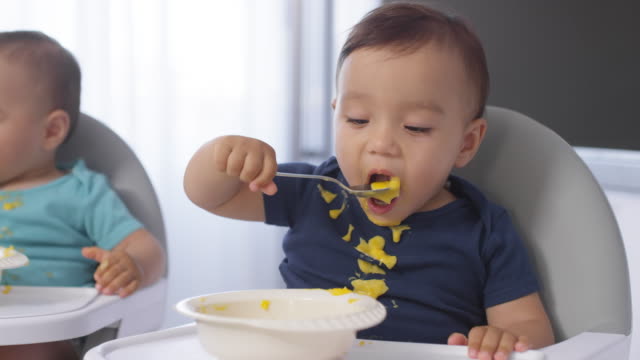 Mellizos-Asiáticos-Desordenados-Comer-Baby-Puree-con-Cucharas