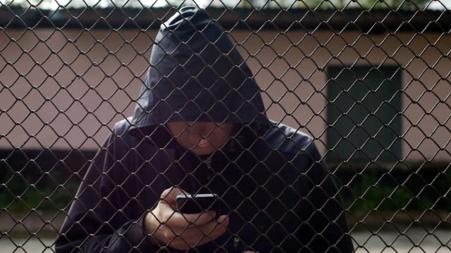 The-imprisoned-hacker-stands-behind-bars-and-climbs-in-the-phone,-hacking-computer-programs,-stealing-through-the-Internet,-hacking-accounts