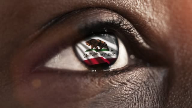 Frau-schwarzes-Auge-in-Nahaufnahme-mit-der-Flagge-des-kalifornischen-Staates-in-Iris,-vereinigte-Staaten-von-Amerika-mit-Windbewegung.-Videokonzept