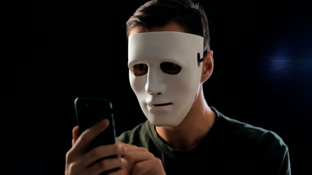 Anonymer-maskierter-Betrüger-fordert-ein-Lösegeld-für-Erpressung-mit-einem-Smartphone.-Maskierter-Krimineller-schüchtert-das-Opfer-mit-Hilfe-von-Drohungen-per-SMS-per-Handy-ein.