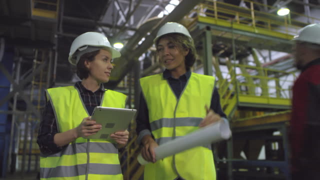 Zwei-Ingenieurinnen,-die-durch-die-Fabrik-laufen-und-reden