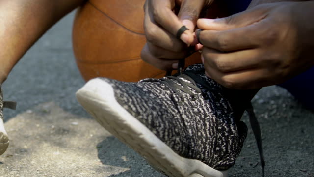 Afro-american-basketball-player-tying-his-shoelaces-before-the-game,-close-up