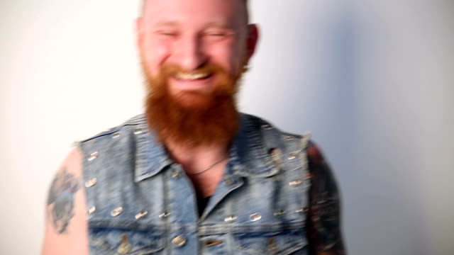 modern-youth.-a-cheerful-portrait-of-a-kindly-laughing-biker-with-tattoos-and-a-stylish-beard-and-mustache-in-a-denim-vest.