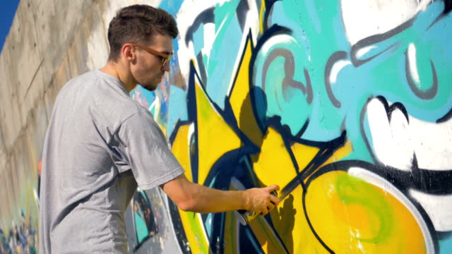 Graffiti-Künstler-malt-ein-schwarzes-Dreieck-auf-den-gelben-Buchstaben,-Ansicht-von-rechts.