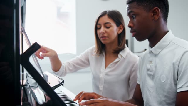 Männliche-Schüler-mit-Lehrer-im-Musikunterricht-Klavier-zu-spielen
