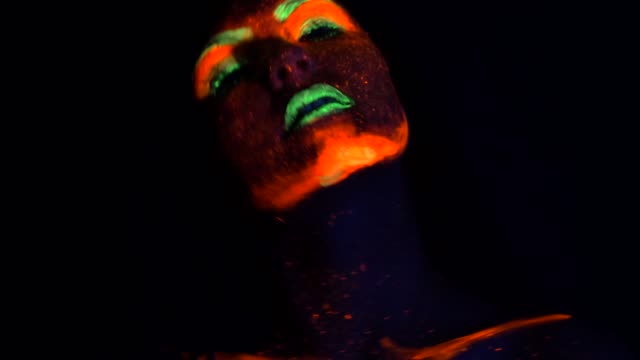 Fashion-sexy-dancer-with-braids-in-neon-light.-Fluorescent-makeup-glowing-under-ultraviolet-light.-Party,-halloween-psychedelic-concepts.-Creative-makeup-looks-great-for-nightclubs
