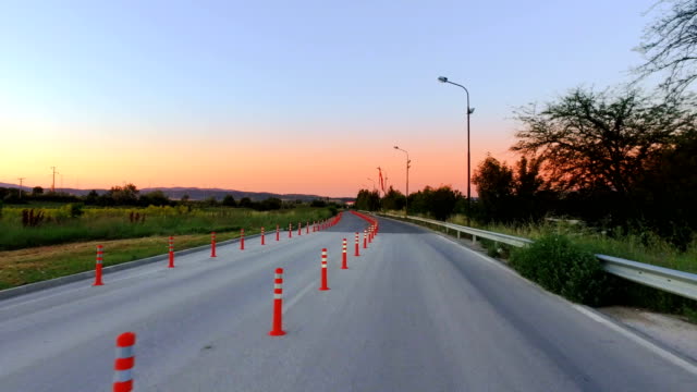 Conducción-a-través-de-un-solo-carril-camino-trabajo-zona-marcadas-con-conos-de-tráfico-en-la-salida-del-sol,-puesta-del-sol