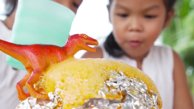 Dos-niñas-asiáticas-hacen-el-experimento-de-volcán-de-bicarbonato-de-sodio-y-vinagre-en-la-mesa-en-su-casa,-lenta-en-50-fps