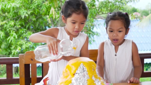 Dos-niñas-asiáticas-hacen-el-experimento-de-volcán-de-bicarbonato-de-sodio-y-vinagre-en-la-mesa-en-su-casa,-lenta-en-50-fps