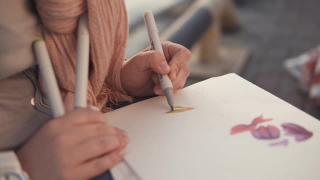Mujer-es-dibujando-motivos-florales-en-un-sketchbook,-sentado-en-un-jardín,-primer-plano