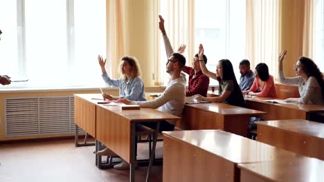 Amable-maestro-está-hablando-a-los-estudiantes-hacer-preguntas-mientras-los-jóvenes-están-levantando-las-manos-y-respondiendo-a-sentarse-en-el-escritorio.-High-School-secundaria,-la-educación-y-concepto-de-la-juventud.