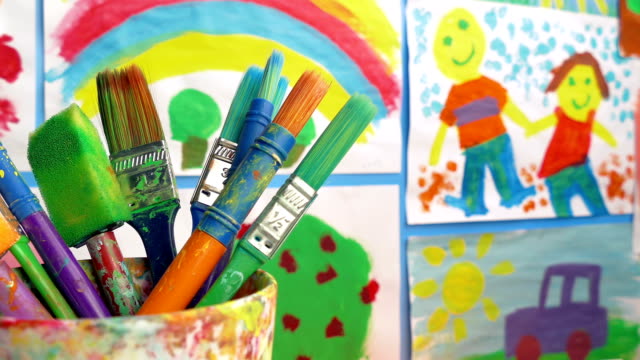 Paint-Brushes-In-Classroom-With-Paintings-On-Wall