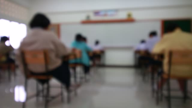 Behind-girls-group-undergraduate-students-testing-of-examination-in-room-and-student-sitting-on-row-chair-doing-final-exams-in-classroom-with-Thailand-uniform.-Asian-Education-Concept.-Top-View.