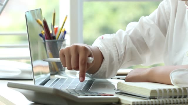 Student-Online-Studie-Lernkonzept:-schöne-Asiatin-lernen-und-schreiben-im-Lehrbuch-oder-Hausaufgaben,-kurze-Notizen-mit-Laptop,-Bleistifte-Box-auf-Schreibtisch-im-Hause-für-e-Learning-in-der-Nähe-von-Fensterhintergrund