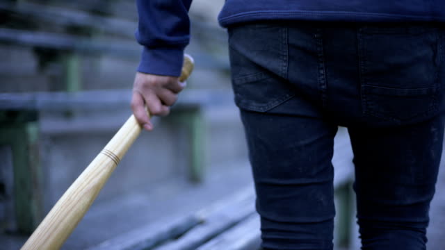 Young-man-walking-on-stadium-tribune-with-baseball-bat,-youth-gang,-vandalism