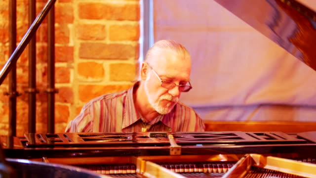 Ein-Grauhaariger-Mann-mit-einem-Schweif-auf-dem-Kopf-tragen-einer-Brille-begeistert-und-nachdenklich-spielt-das-Klavier-in-einer-jazz-bar