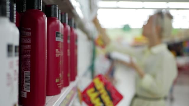 Mujer-joven-borrosa-elegir-acondicionador-o-shampoo-en-una-tienda-de-belleza.-Mujer-que-sostiene-un-producto-de-cuidado-del-cuerpo
