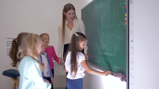 Schüler-und-Lehrer-am-Whiteboard-im-Klassenzimmer,-Schülerin-nimmt-Stück-Kreide-und-schreibt-Antwort-im-Unterricht