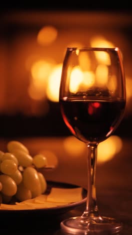 Vertical-video-of-one-red-wine-wineglasses-over-fireplace-background.