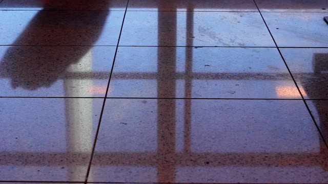 Floor-reflection-of-man-walking-with-carry-on-luggage-at-airport-terminal
