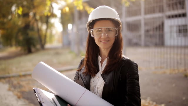 Portrait-of-Happy-professional-construction-engineer-woman-holding-the-blueprint-and-wearing-the-safety-helmet-and-glasses.