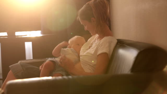 Young-mother,-breastfeeding-on-sunset-on-quiet-evening-her-little-baby-boy-in-sunny-living-room