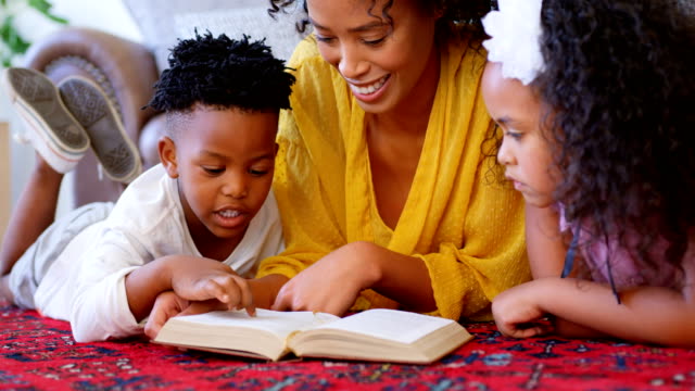 Vista-frontal-de-negro-de-la-madre-con-sus-hijos-leyendo-un-libro-en-un-cómodo-hogar-4k