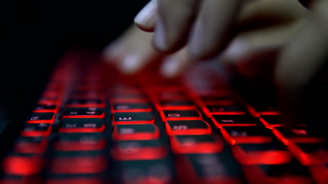 Adolescente-hacker-Girl-ataca-servidores-corporativos-en-Dark,-escribiendo-en-el-teclado-del-ordenador-portátil-rojo-iluminado.-Habitación-es-oscura
