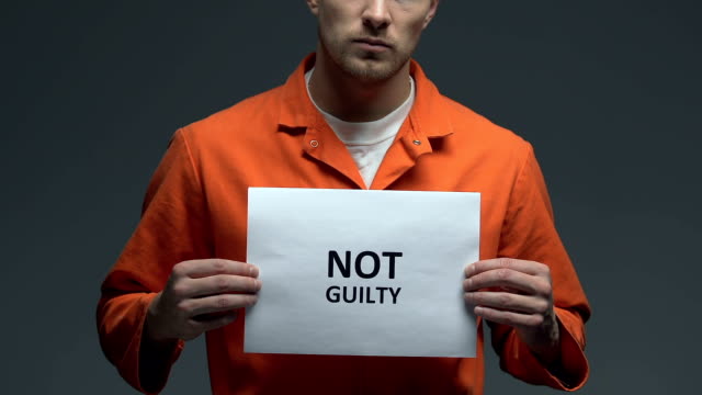 Not-guilty-phrase-on-cardboard-in-hands-of-Caucasian-male-prisoner,-innocent