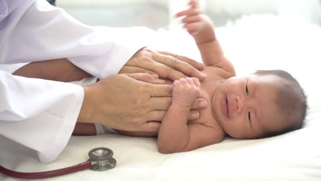 4K-Medium-close-up-shot-female-pediatrician-doctors-hand-consoling-crying-asian-newborn-baby-girl-using-stethoscope-listening-to-little-baby-girl-heartbeat-for-medical-exam.-Hospital-nursery-healthcare-concept.