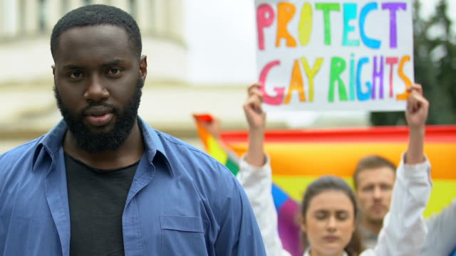 Black-man-raising-rainbow-heart-together-with-protesters-for-LGBT-rights,-rally