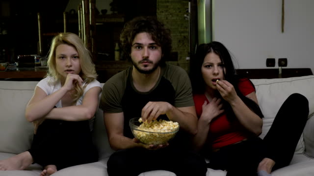 Zwei-junge-Frauen-und-ein-Mann-Essen-Popcorn-und-Horror-Film-mit-einer-Angst-vor-grim-auf-ihrem-Gesicht-zu-beobachten