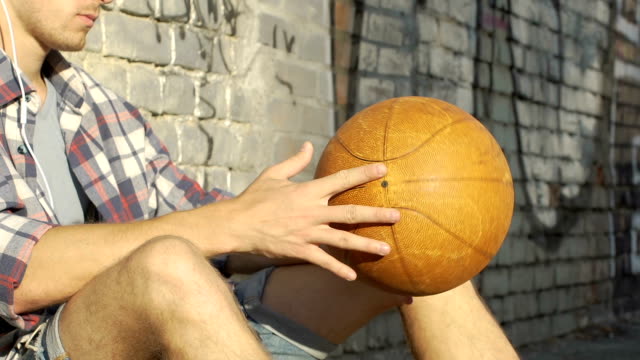 Junger-Mann-anhören-von-Musik-und-Basketball-in-Händen,-spinning-Freunde-warten