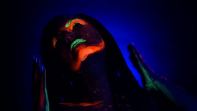 Fashion-model-woman-with-braids-dancing-in-neon-light.-Fluorescent-makeup-glowing-under-UV-black-light.-Night-club,-party,-halloween-psychedelic-concepts
