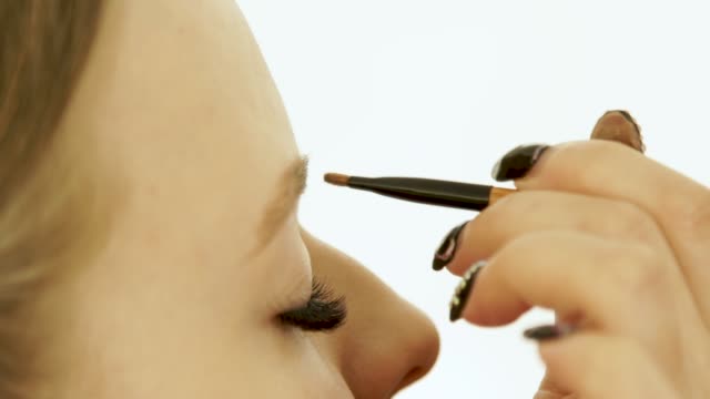 Frau-Gesicht-während-Augenbrauen-Make-up-im-Kosmetikstudio-hautnah.-Frau-genießt-mit-Make-up-Pinsel-zum-Färben-von-Augenbrauen-über-Schönheit-gesichtsmodell-in-Umkleidekabine