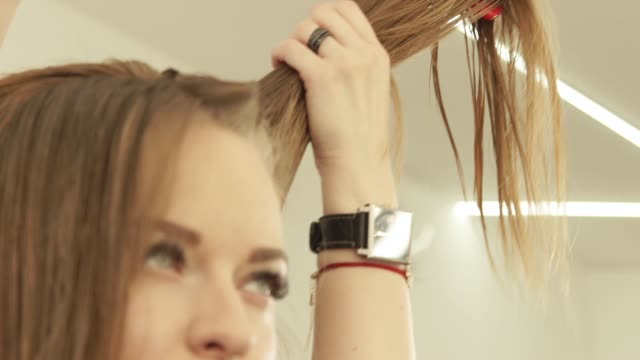 Woman-hairdresser-combing-strand-hair-with-hairbrush-during-cutting-in-beauty-salon.-Close-up-hairdresser-making-female-haircut-in-hairdressing-salon