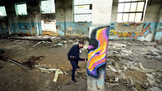 High-angle-shot-of-young-urban-painter-creating-abstract-image-on-column-in-old-damaged-building.-Modern-art,-street-artist,-creativity-and-people-concept.