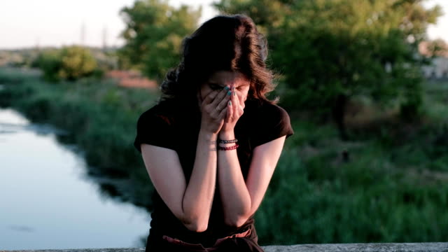 A-view-from-left-to-right-of-a-sad,-bitterly-crying-woman,-standing-on-a-bridge