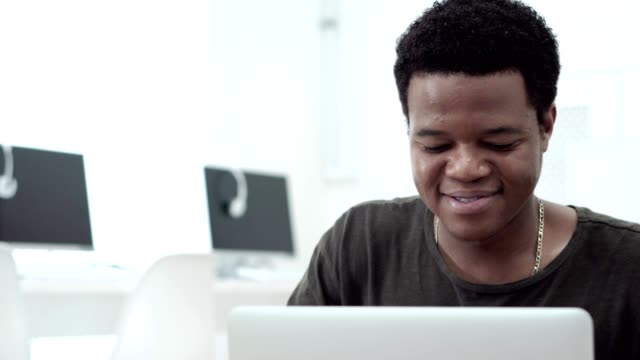 Handsome-Black-university-student-smiling-and-laughing-while-working-on-laptop-in-computer-classroom