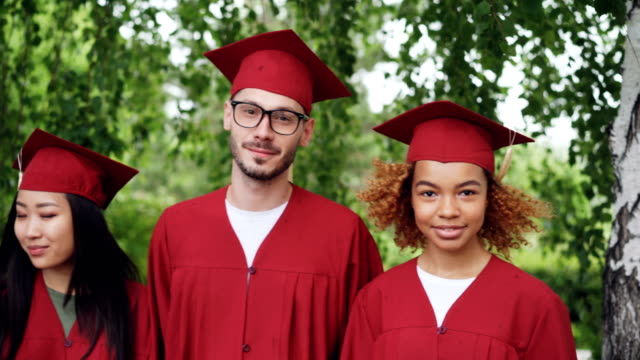 Retrato-de-un-grupo-multinacional-de-estudiantes-graduados-en-vestidos-de-graduación-rojos-y-mortero-paneles-juntos-al-aire-libre-de-pie,-sonriendo-y-mirando-a-cámara.