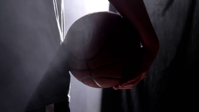 Close-footage-of-basketball-player-holding-ball,-standing-in-dark-misty-room