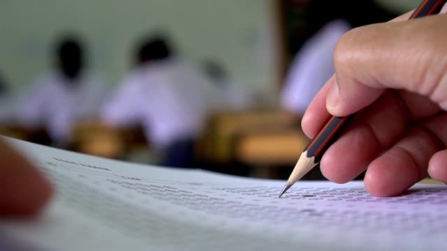Bildung-Testkonzept:-Hände-Schüler-halten-Stift-für-Prüfung-Prüfungen-schreiben-Antwortbogen-oder-Übung-für-die-Aufnahme-in-Prüfung-Kohlepapier-Computer-auf-Holztisch-im-Klassenzimmer-in-der-High-School-zu-füllen