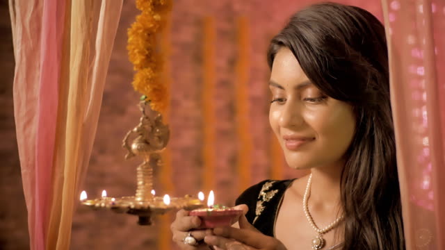 Eine-gut-aussehende-Frau-in-einen-Sari-Lichter-der-hängenden-Öl-Lampe-und-lächelt-in-die-Kamera-schauen