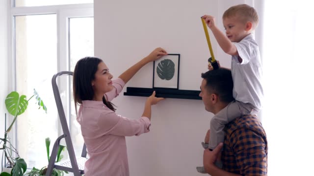 Renovierung-nach-Hause,-junges-Paar-mit-kleinen-Jungen-hängen-Gemälde-an-der-Wand-beim-Umbau-im-apartment