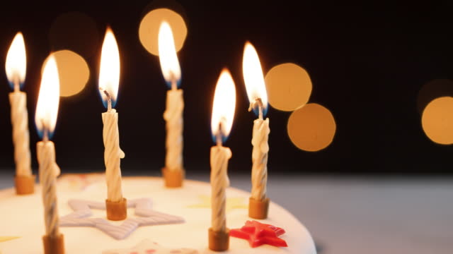 Close-up-of-lit-candles-on-a-white,-decorated-birthday-cake,-bokeh-lights-in-the-background