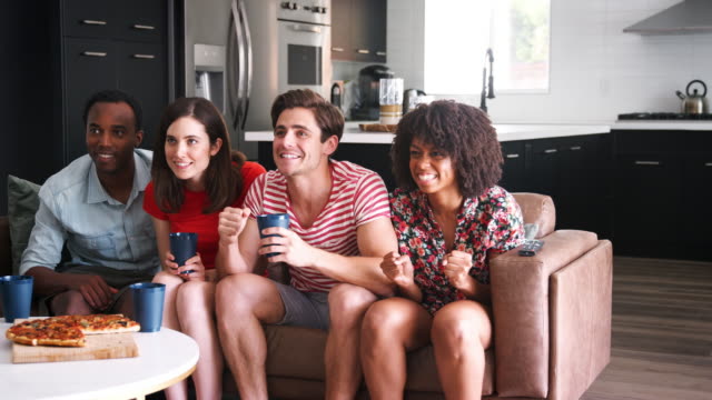 Four-young-adult-friends-watching-sports-on-TV-celebrating