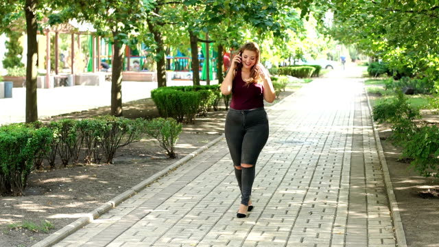 Ein-junges-Mädchen-mit-Übergewicht-Spaziergänge-im-Park-und-am-Telefon-zu-sprechen.